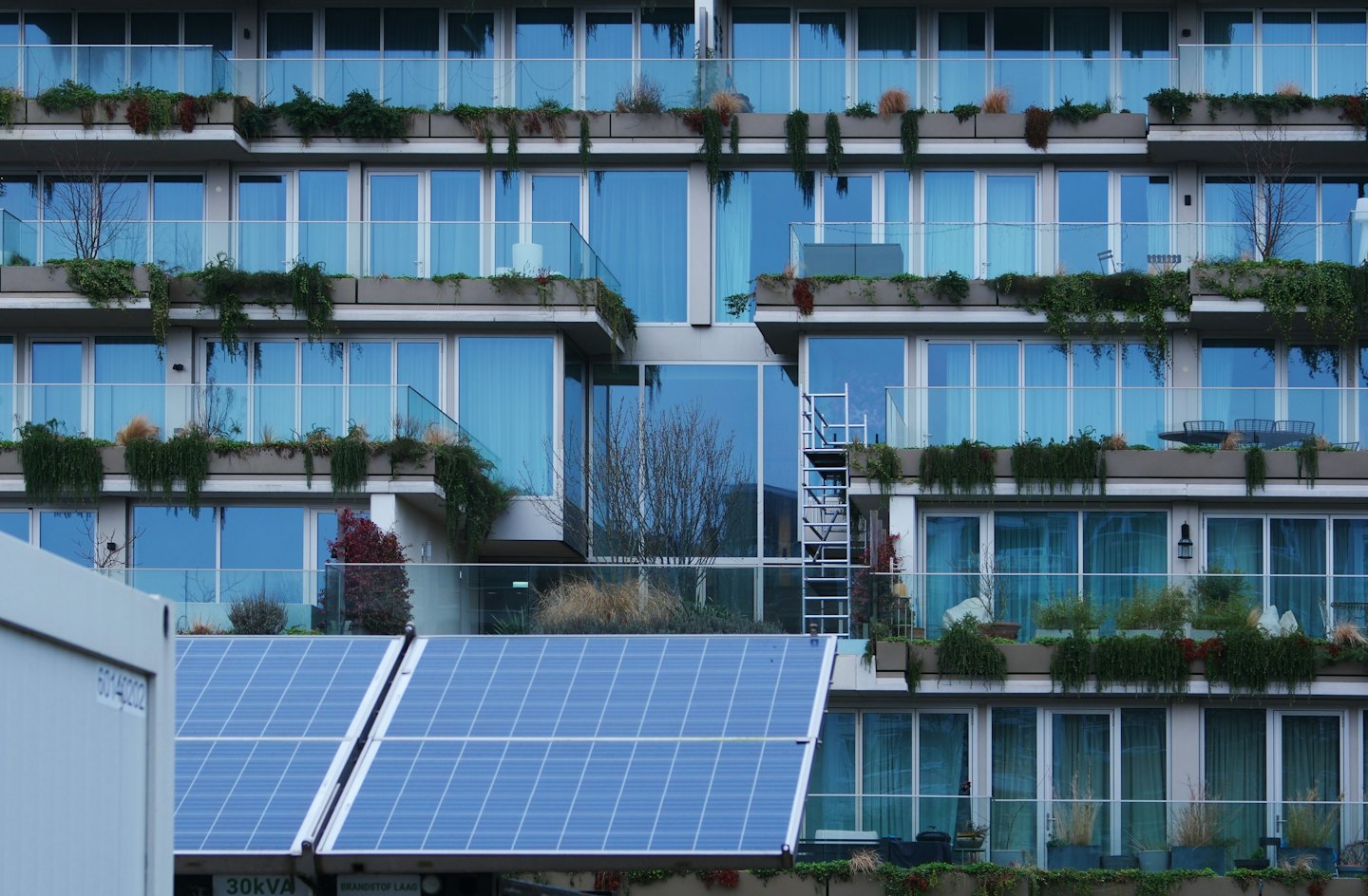 Immeuble d'appartements avec balcons, verdure et panneaux solaires.